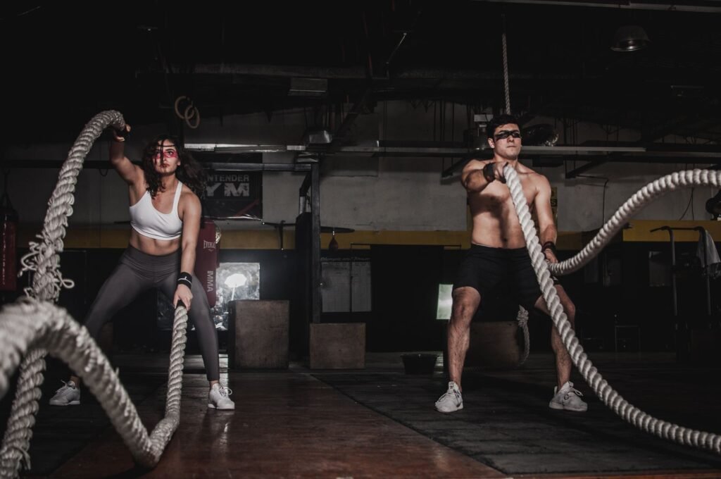 Dos atletas entrenando con cuerdas de batalla en un gimnasio HYROX equipado para entrenamiento funcional