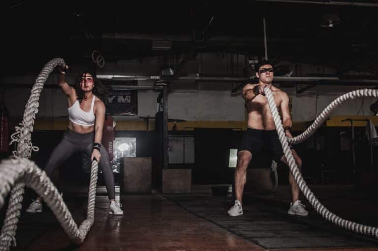Dos atletas entrenando con cuerdas de batalla en un gimnasio HYROX equipado para entrenamiento funcional